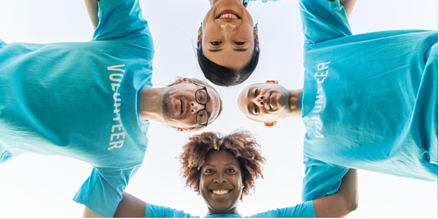 Two men & two women in blue volunteer t-shirts looking downwards into a camera shot