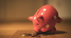 Pink ceramic piggy bank on a brown table, with a small pile of coins