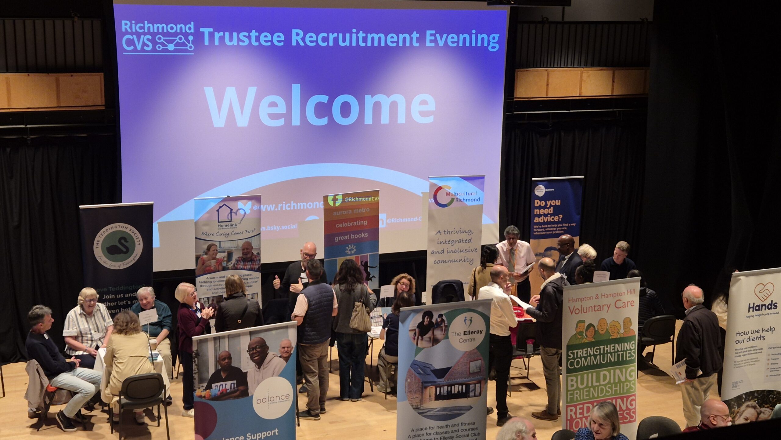 2026 Trustee Recruitment Evening stallholders and visitors in Theatre at RHACC with large Welcome slide projection