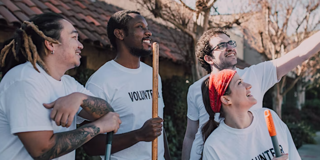 Mixed group of young people with brooms and 'volunteer' t-shirts taking a selfie on a street