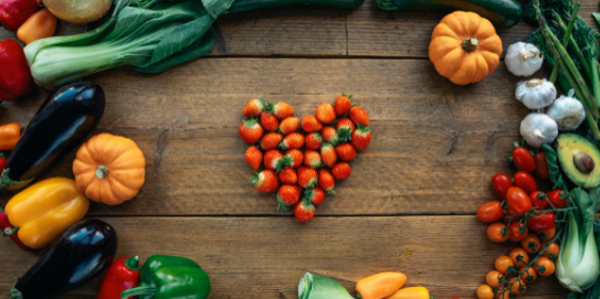 A selection of bright coloured fruit and veg on a wooden table with a heart shape of strawberries in the centre