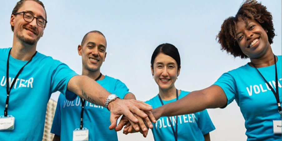Mixed group of people in bright blue t-shirts with the word Volunteer on them joining hands