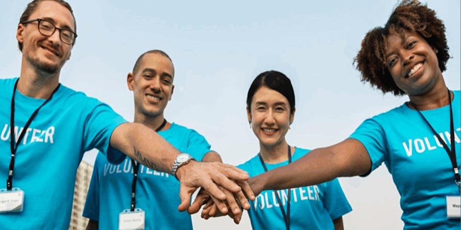 Mixed group of people in bright blue t-shirts with the word Volunteer on them joining hands