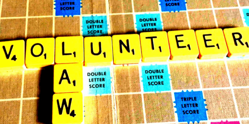 Letters on a Scrabble board with intersecting words 'volunteer' and 'law'