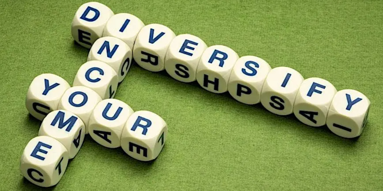 Lettered dice on a green fabric surface in a crossword style formation, spelling out Diversify Your Income