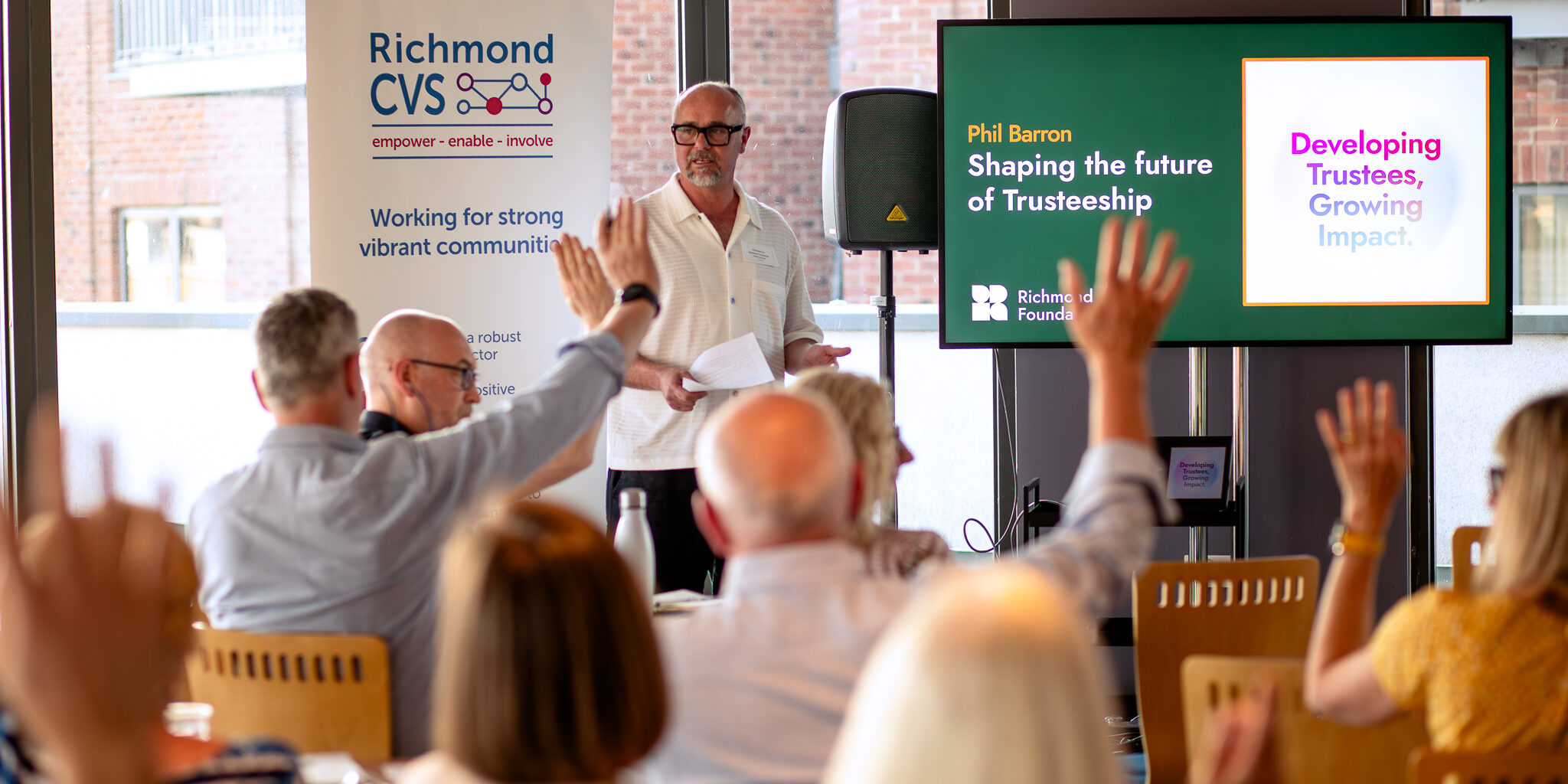 CEO of Richmond Foundation standing and presenting at Trustee Forward launch event , with Richmond CVS banner and Richmond Foundation / Trustee Forward slide in background